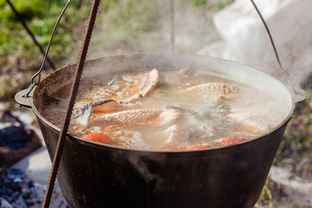 Tasty fish soup in cauldron with smoke outdoors